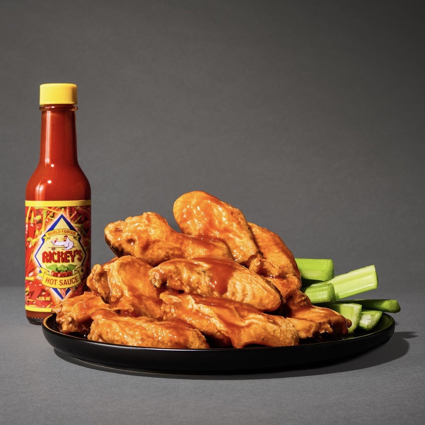 Platter of wings with celery sticks and a bottle of Rickey's on a gray background