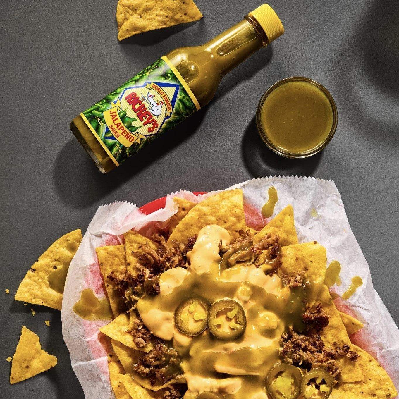 Nachos with a bottle of Rickey's Jalapeño Sauce on a gray surface